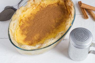 Milk tart with cinnamon sticks and cinnamon shaker close up