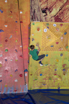 The boy clambers up on the rock climbing wall