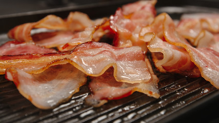 CLOSE UP: Many strips af bacon on a black pan