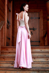 Fototapeta premium Fine emotional brunette on old style veranda, full length. Yonge girl in vintage pink pastel with live expressions on beautiful country and old background.