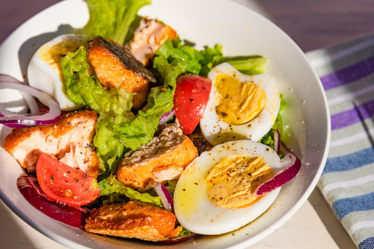 Healthy diet salad with salmon, tomatoes, eggs, onion and lettuce, top view. Dietary lunch