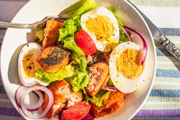 Paleo diet salad with salmon, tomatoes, eggs, onions and lettuce, close-up