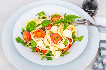 Italian food - Spaghetti caprese close-up. Pasta with mozzarella, cherry tomatoes and basil