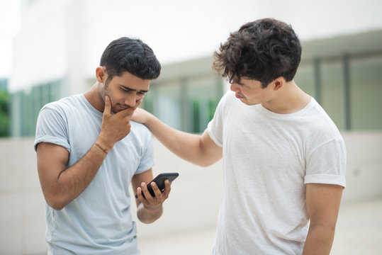 Disappointed Indian guy receiving bad news via sms, his friend supporting him. Curly-haired guy touching shoulder of friend while consoling him outdoors. Distraught concept - Powered by Adobe