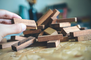 Closeup image of a hand holding and playing Jenga or Tumble tower wooden block game