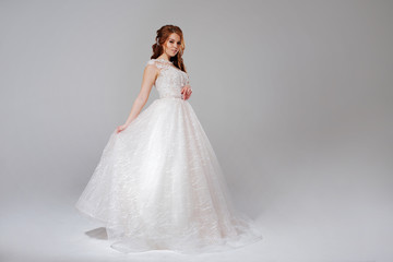 Fototapeta na wymiar Lovely young woman bride in lavish wedding dress. Light background.