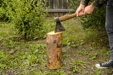 A man splits a log with an ax against the background of a wooden fence