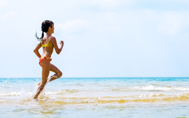 Summer fun beach woman splashing water. Panorama landscape of tropical ocean on travel holiday. Bikini girl running in freedom and joy with hands up enjoying the sun.