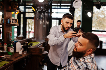 Handsome bearded man at the barbershop, barber at work, making photo on his phone.