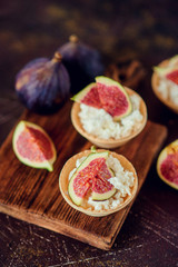 Autumn dessert: tartlets baskets with ripe figs, soft cheese and honey on a light background.