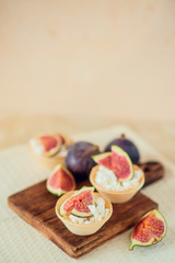 Autumn dessert: tartlets baskets with ripe figs, soft cheese and honey on a light background.