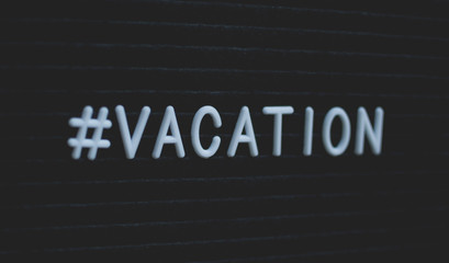 Hashtag word #vacation written on the letter board. White letters on the black background.
