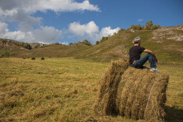 Naklejka na ściany i meble a man resting after work on a haystack in a field with a harvested crop