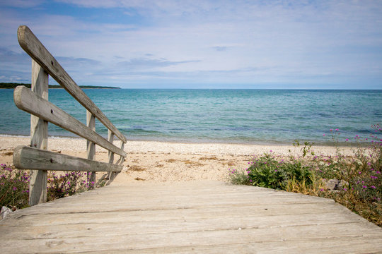 Path To The Beach. Wooden ramp leads to a wide sandy beach with a blue water horizon on a sunny sandy beach along the Great Lakes coast. 