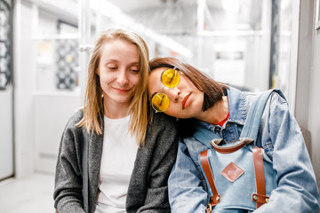 Young woman sleeping on the shoulder of her girl friend in the metro train, friendship and...