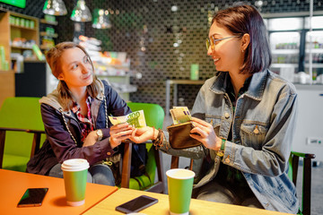 A woman gives to a stranger person or her friend euro banknote money in the interior of a cafe. The concept of lending money or fraud