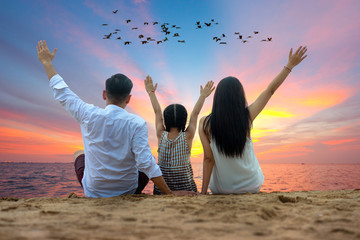 Happy asian family - father, mother, kid hold hands up in the air together with fun along sunset sea beach. Travel, active lifestyle, parents with children on summer vacations with flock of birds