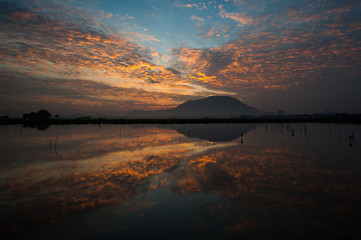 Fototapeta premium Dramatic sunrise with beautiful cloud over a hill with reflection in the foreground