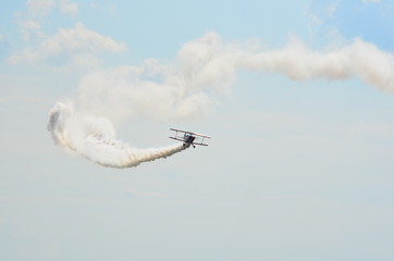 Stunt biplane flying on cloudy blue sky leaving white smoke trail