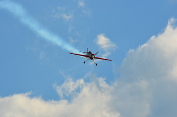 Stunt monoplane flying on cloudy blue sky leaving white smoke trail