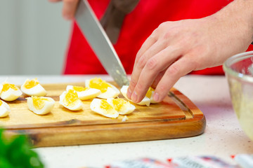 Man cuts boiled quail eggs on wooden cutting board close-up. Step by step recipe of homemade tuna salad.