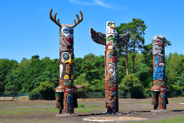 Three colorful wooden totem poles on green trees and blue sky background outdoors in park.