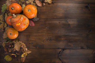 Happy Halloween! The concept of the holiday, autumn still life of small pumpkins that lie on dry leaves on a dark wooden background. One pumpkin carved lantern. Border, top view, copy space