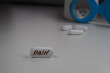 white oval tablet with the inscription "pain" and an open jar of tablets in the background
