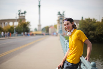 Young man in yellow t-shirt waiting on a bridge.