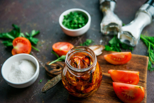 Appetizer, delicacy: preparation of dried tomatoes in a jar with spices, on a dark background.