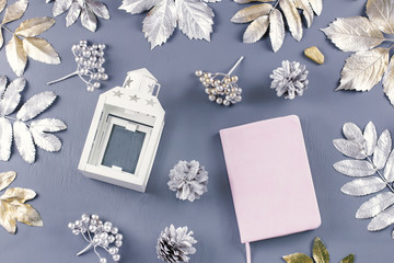 Winter concept flat lay with lantern, note book, candles and silver leaves.
