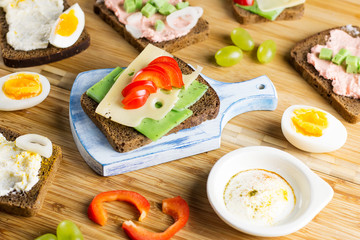 Breakfast table with cheese sandwiches, sausage, vegetables, hard boiled eggs and fruits