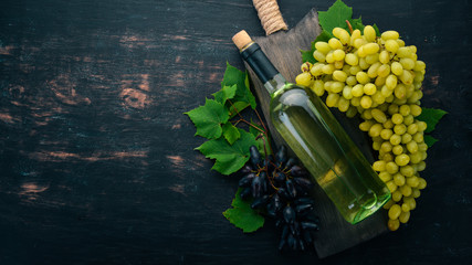 A bottle of white wine on a black wooden background. Grape. Free space for text. Top view.