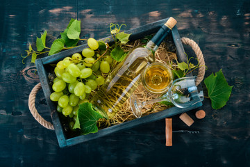 A bottle of white wine with glasses and grapes. Leaves of grapes. Top view. On a black wooden background. Free space for text.