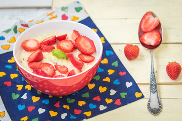 Homemade porridge with strawberries in a red bowl on the heart pattern cloth napkin with  spoon aside.