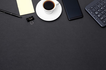 Business flat lay: high angle view of office black desk with copy space. Table with keyboard, smartphone, coffee cup and supplies. Top view of blackboard office desk. Businessman or student desk.