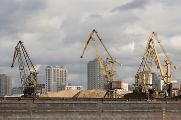 Fototapeta na wymiar A barge in the river port and working cranes on the city background