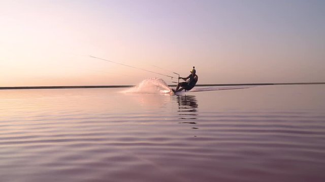 A man on a pink lake kitesurfing, sailing to the camera. Slow motion