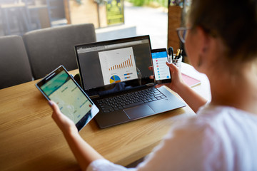 Mixed race woman in glasses working with multiple electronic internet devices. Freelancer...