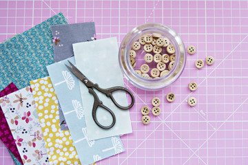 Wooden buttons in jar, retro scissors, cotton fabric scraps and pink cutting mat