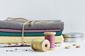 Fototapeta na wymiar Vintage thread spools, pins, little wooden buttons, metal jar and cotton fabrics on white