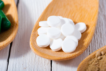 medicament pills on bamboo spoon, white wood table