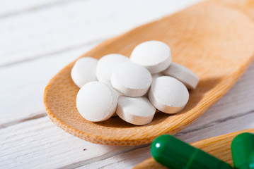 medicament pills on bamboo spoon, white wood table