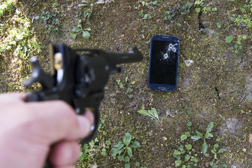 A man's hand with a pistol shoots at a mobile phone.