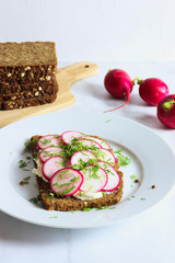 Slice of whole grain rye bread with cream cheese, radishes and dill