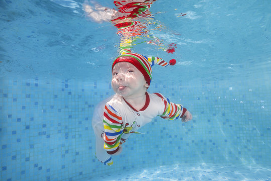  3 months boy in a bright striped swimming suit swims underwater in the pool