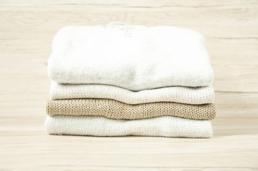 Pile of knitted winter sweaters on wooden background.