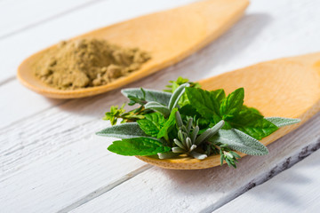 herbal leaves and ground herb powder on bamboo spoons, white wooden table