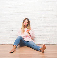 Fototapeta na wymiar Young adult woman sitting on the floor over white brick wall smiling with hands on chest with closed eyes and grateful gesture on face. Health concept.