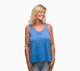 Middle age blonde woman over isolated background looking away to side with smile on face, natural expression. Laughing confident.